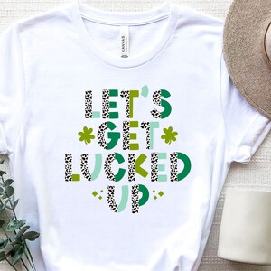 May include: White t-shirt with a green, black, and white graphic that says "Let's Get Lucked Up".