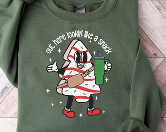 Könnte beinhalten: Grünes Sweatshirt mit einem Cartoon-Weihnachtsbaum, der eine Tasche trägt und eine Tasse hält. Der Text auf dem Sweatshirt lautet "out here lookin' like a snack".
