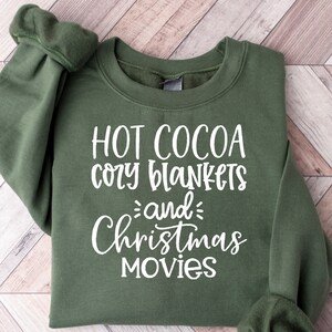May include: A green sweatshirt with the text "HOT COCOA cozy blankets and Christmas movies" in white.