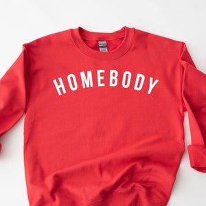 May include: Red sweatshirt with the text "HOMEBODY" in white lettering.