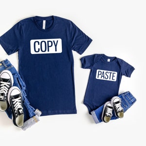 May include: A navy blue t-shirt with the word "COPY" printed on it and a navy blue bodysuit with the word "PASTE" printed on it. Both shirts have white text.