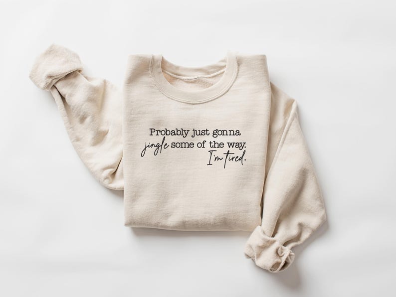 Puede incluir: Sudadera color crema con el texto "Probably just gonna jingle some of the way. I'm tired." en escritura negra. Las mangas est&aacute;n enrolladas. Una prenda casual y c&oacute;moda, ideal para el uso diario.