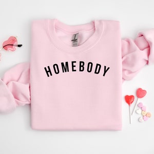 May include: Pink sweatshirt with the text "HOMEBODY" in black lettering.