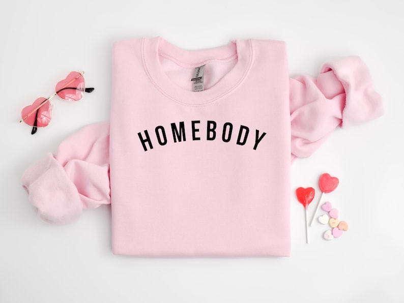 May include: Pink sweatshirt with the text "HOMEBODY" in black lettering.