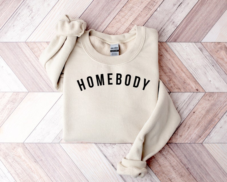 May include: A beige sweatshirt with the text "HOMEBODY" printed in black on the front.