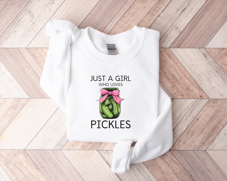 Puede incluir: Sudadera blanca con el texto "Just a girl who loves pickles" y un dibujo de un tarro de pepinillos con un lazo rosa.
