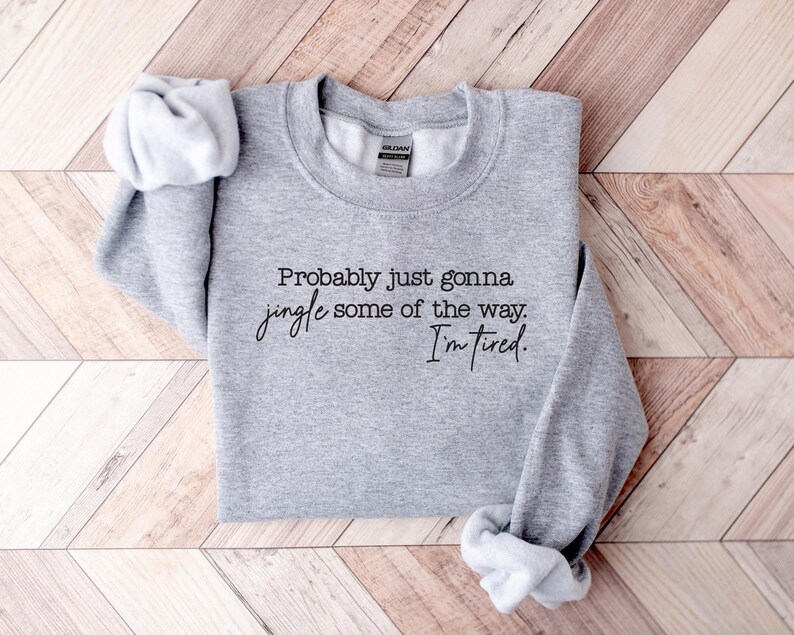 Puede incluir: Una sudadera gris jaspeada con el texto "Probably just gonna jingle some of the way. I'm tired." en escritura negra. La sudadera est&aacute; doblada, con las mangas visibles.