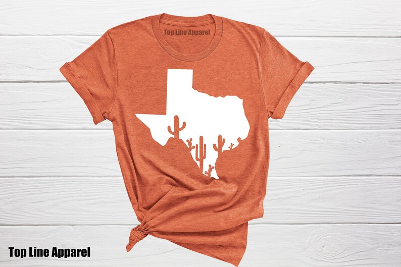 May include: A rust-colored t-shirt with a white outline of the state of Texas and cactus silhouettes. The text "Top Line Apparel" is printed on the shirt.