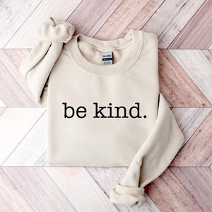 May include: A beige sweatshirt with the text "be kind." printed in black.