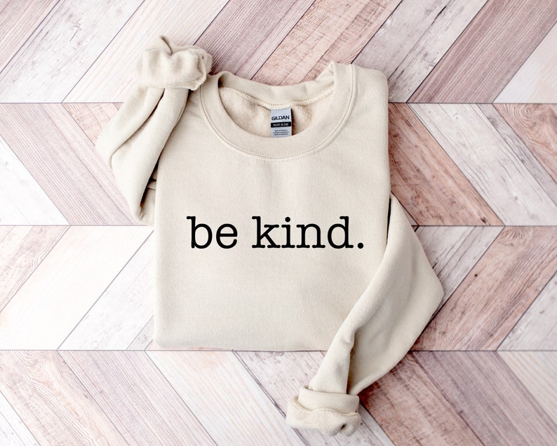 May include: A beige sweatshirt with the text "be kind." printed in black.