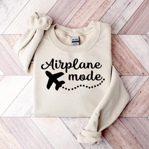 May include: A beige sweatshirt with black text that reads "Airplane mode" and a small airplane graphic with a dotted line trailing behind it.