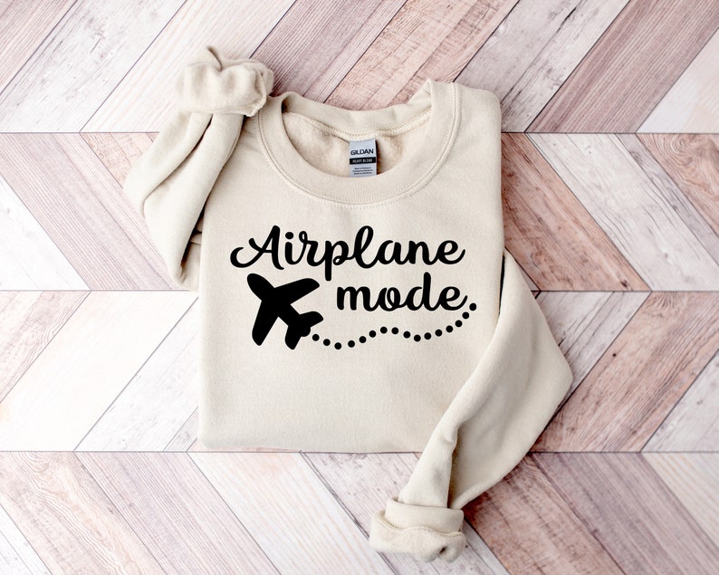 May include: A beige sweatshirt with black text that reads "Airplane mode" and a small airplane graphic with a dotted line trailing behind it.