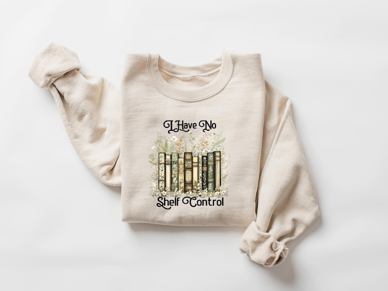 May include: Beige sweatshirt with the text "I Have No Shelf Control" in black script. The graphic features a stack of books with floral accents. The sweatshirt is made of a soft material and has long sleeves.