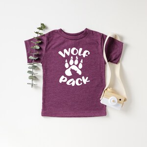 May include: A maroon toddler t-shirt with white text that reads "Wolf Pack" and a white wolf paw print.