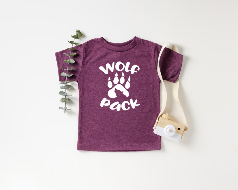 May include: A maroon toddler t-shirt with white text that reads "Wolf Pack" and a white wolf paw print.