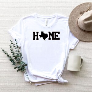 May include: White t-shirt with a black outline of the state of Texas and the word "HOME" printed on it.