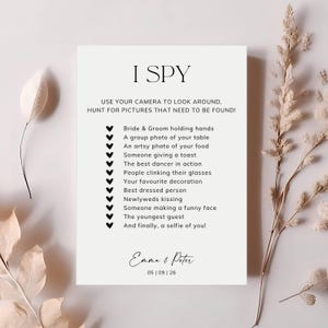 May include: A white rectangular wedding I Spy game card with black text and heart icons. The card lists photo prompts for guests and features the names Emma & Peter with the date 05 | 09 | 26 at the bottom in a clean, black serif font.