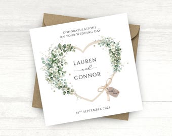 Op de afbeelding: Trouwkaart met een hartvormig bloemendesign, met de namen "Lauren en Connor" en de datum "15 september 2025". De kaart ligt op een bruine envelop, met de tekst "Gefeliciteerd met jullie bruiloft".