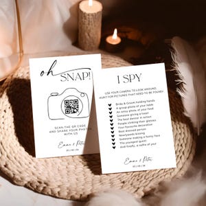 May include: Two white rectangular wedding cards with black text. One card features the text oh SNAP! with a camera icon containing a QR code, and the other lists an I SPY game with a checklist of photo tasks. Both cards are personalised with Emma & Peter and the date 05 | 09 | 26.
