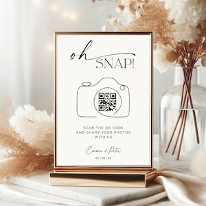 May include: A rectangular sign in a gold frame featuring the text oh SNAP! above a line-art camera icon containing a QR code. Below the camera, the text reads SCAN THE QR CODE AND SHARE YOUR PHOTOS WITH US, followed by Emma & Peter and 05 | 09 | 26.