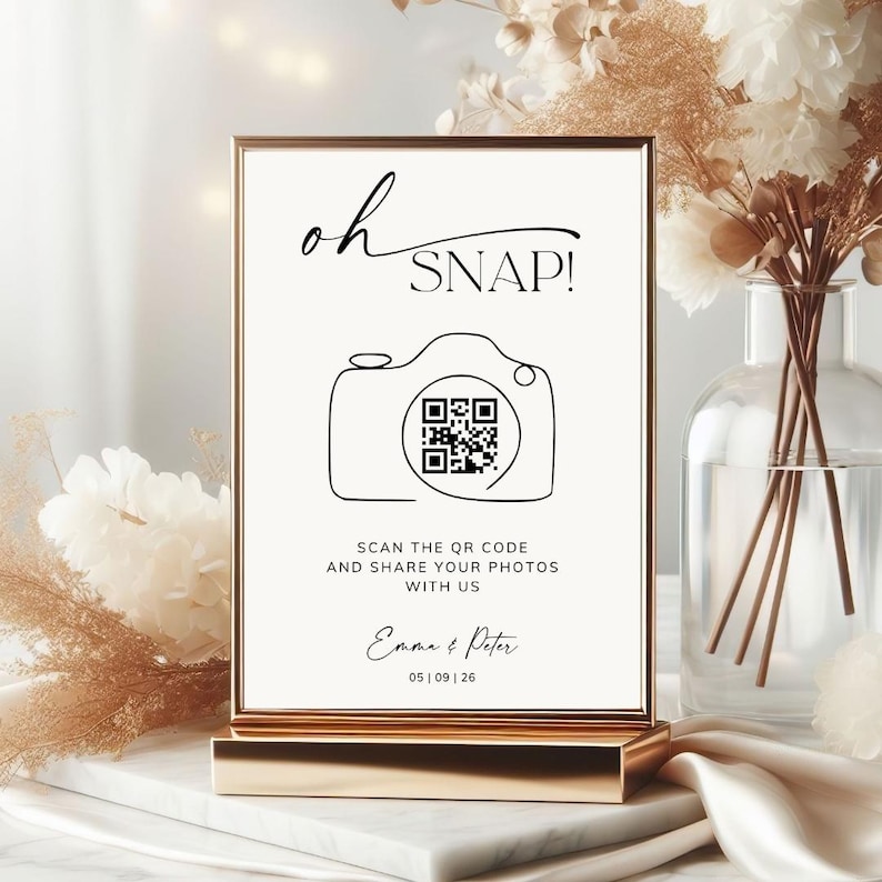 May include: A rectangular sign in a gold frame featuring the text oh SNAP! above a line-art camera icon containing a QR code. Below the camera, the text reads SCAN THE QR CODE AND SHARE YOUR PHOTOS WITH US, followed by Emma & Peter and 05 | 09 | 26.