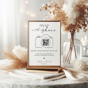May include: A gold-framed sign with the text "SNAP and share" and a camera graphic. The sign reads "SHARE YOUR PHOTOS WITH US! SCAN THE QR CODE AND UPLOAD YOUR BEST PHOTOS!" with a QR code and the names "Jessica & Samuel" and the date "06|09|25".