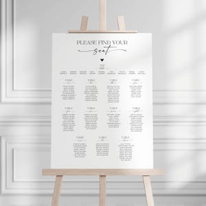 May include: A white wedding seating chart sign on a wooden easel with black text that reads Please Find Your Seat, Top Table, and lists guest names organised by table numbers one through eleven in a clean, minimalist sans-serif font.