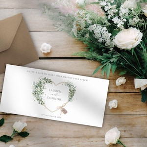 Op de afbeelding: Een trouwuitnodigingskaart met een hartvormig bloemendesign, de namen "Lauren en Connor" en de datum "16 september 2023". De kaart ligt op een houten oppervlak met een boeket witte rozen en groen, en een bruine envelop.