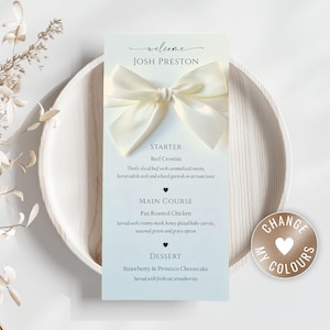 May include: A wedding menu card with a cream bow, displaying the name "Josh Preston" and a list of dishes. The card is on a white plate, with a "Change My Colours" sticker.