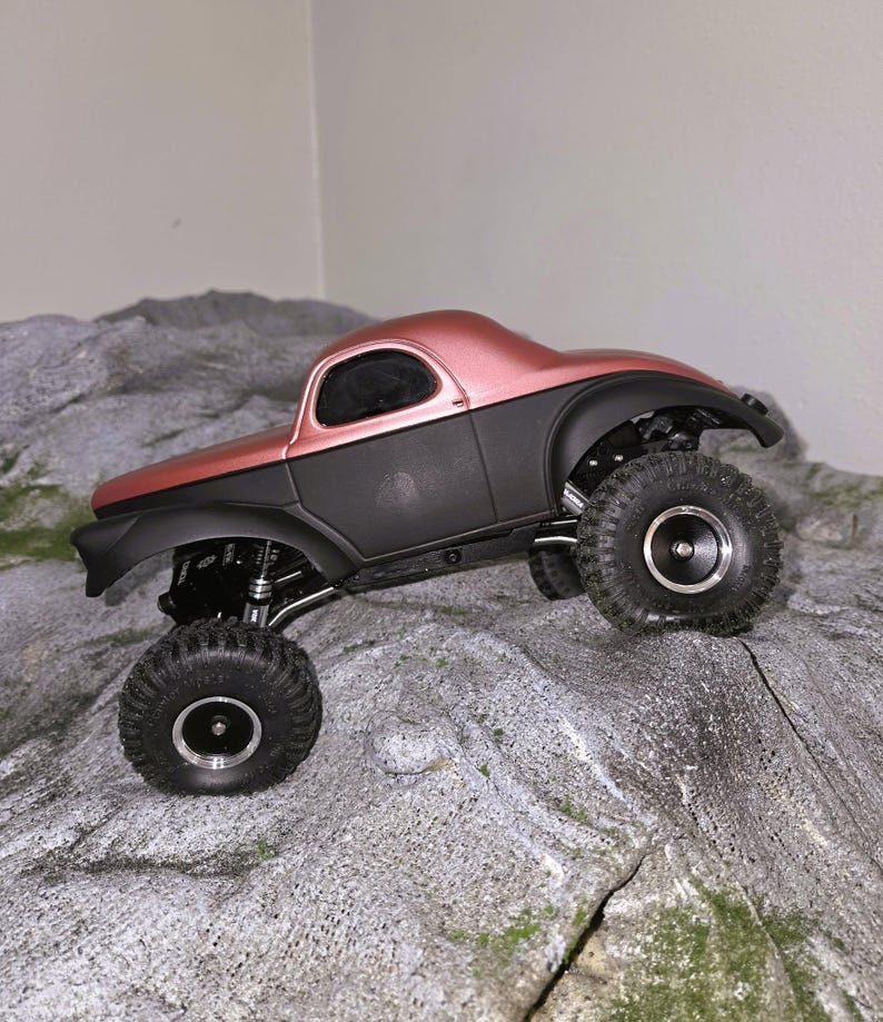 Pu&ograve; includere: Un veicolo radiocomandato di tipo crawler con carrozzeria superiore in oro rosa metallizzato e telaio inferiore nero opaco. Il veicolo &egrave; dotato di grandi pneumatici fuoristrada testurizzati con cerchi argentati e sospensioni a vista.