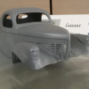 Pu&ograve; includere: Una carrozzeria per modellino d'auto grigia e non verniciata, caratterizzata da una classica silhouette coup&eacute; con parafanghi anteriori prominenti, una griglia verticale e fari arrotondati. Dietro il modello c'&egrave; un cartoncino con la scritta Gasser.