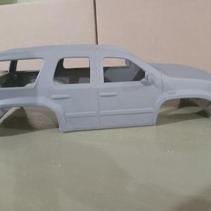Può includere: Una carrozzeria per modellino d'auto in plastica grigia non verniciata con un design da SUV a quattro porte. L'esterno presenta dettagli stampati tra cui cornici dei finestrini, maniglie delle portiere, specchietti laterali e passaruota.
