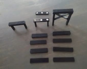 May include: A set of black wooden miniature furniture pieces, including a bench, a table, and a tall structure with a cross-shaped frame. The pieces are arranged on a gray surface.