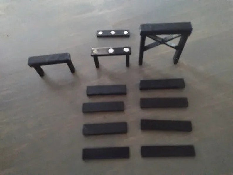 May include: A collection of small, black wooden furniture pieces, including tables and supports. The set includes a small table with two legs, a table with four legs, and a sawhorse-style support. Several rectangular pieces are also present.
