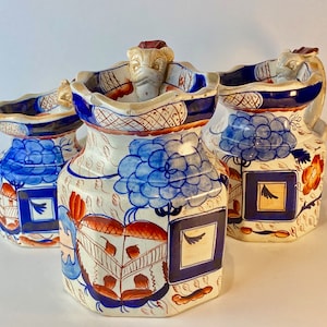 Puede incluir: Tres jarras de cerámica antiguas con motivos florales azules y blancos y acentos rojos. Las jarras tienen una forma octogonal única y presentan un pico en forma de cabeza de león.