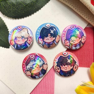May include: Five circular, colourful badges with holographic effects. Each badge displays a cartoon character with a heart above their head and waving paws. The characters have different hair colours and wear suits. The badges are on a white and pink background.