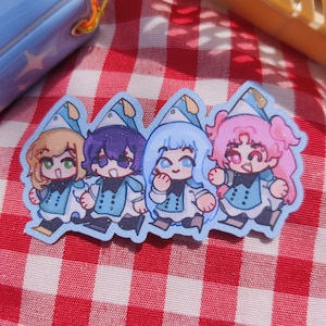 May include: A die-cut sticker featuring four chibi-style characters standing side-by-side. Each character wears a blue and white pointed hat and a matching blue vest with dark buttons. The characters have distinct hair colors: blonde, dark purple, light blue, and pink.