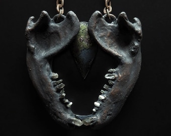 May include: A black metal necklace with a jawbone pendant featuring crystal teeth and a green stone accent.