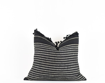 Puede incluir: Almohada de tiro a rayas blancas y negras con borlas negras. La almohada está hecha de un tejido tejido y tiene una forma cuadrada.