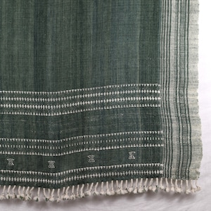 May include: A dark green woven throw blanket with white fringe and a white geometric pattern along the bottom edge.