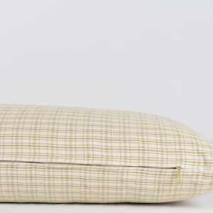 May include: A beige and brown checkered lumbar pillow with a zipper closure.