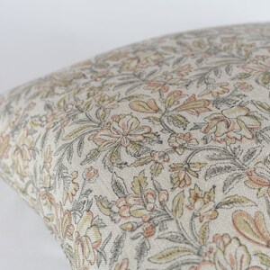 May include: A beige pillow cover with a floral pattern in shades of grey, pink, and yellow.