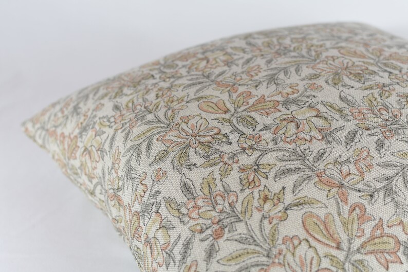 May include: A beige pillow cover with a floral pattern in shades of grey, pink, and yellow.