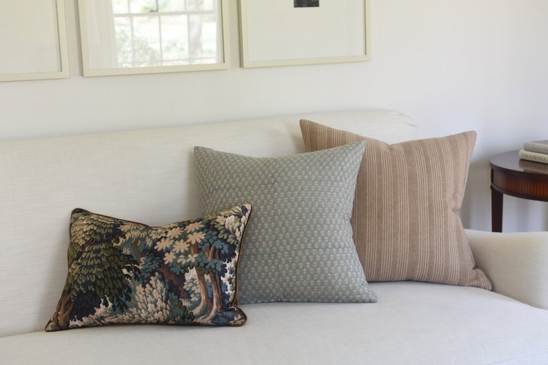May include: Three decorative throw pillows on a white couch. The pillows are a tapestry pattern with trees, a light blue patterned fabric, and a brown and white striped fabric.