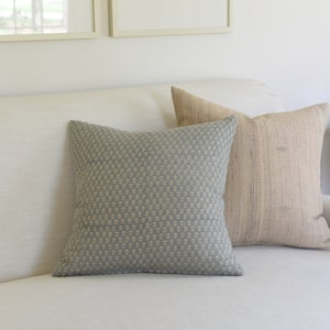 May include: A white sofa with two throw pillows. One pillow is a light blue with a white pattern, and the other is a light brown with a woven texture.