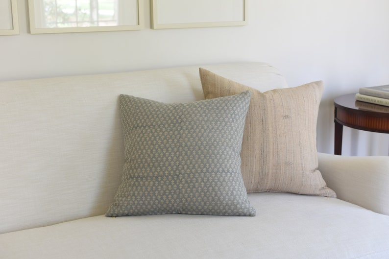 May include: A white sofa with two throw pillows. One pillow is a light blue with a white pattern, and the other is a light brown with a woven texture.