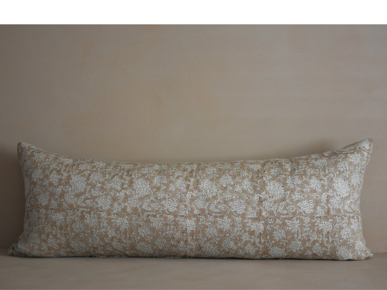 Puede incluir: Una almohada larga y rectangular de tela beige con un patr&oacute;n floral blanco.
