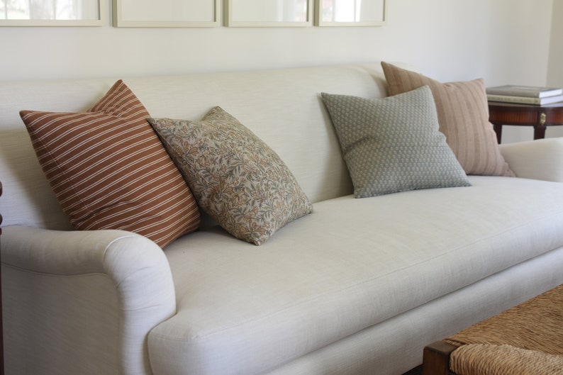 May include: A white linen sofa with a variety of throw pillows. The pillows are brown with white stripes, brown with a floral pattern, and green with a geometric pattern.