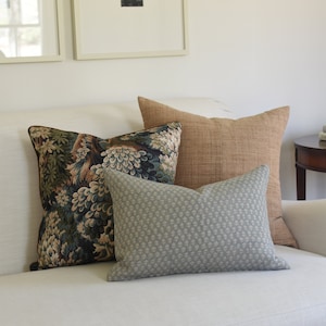 May include: A white couch with three throw pillows. The pillows are a patterned floral design, a solid brown, and a light blue with a small geometric pattern.