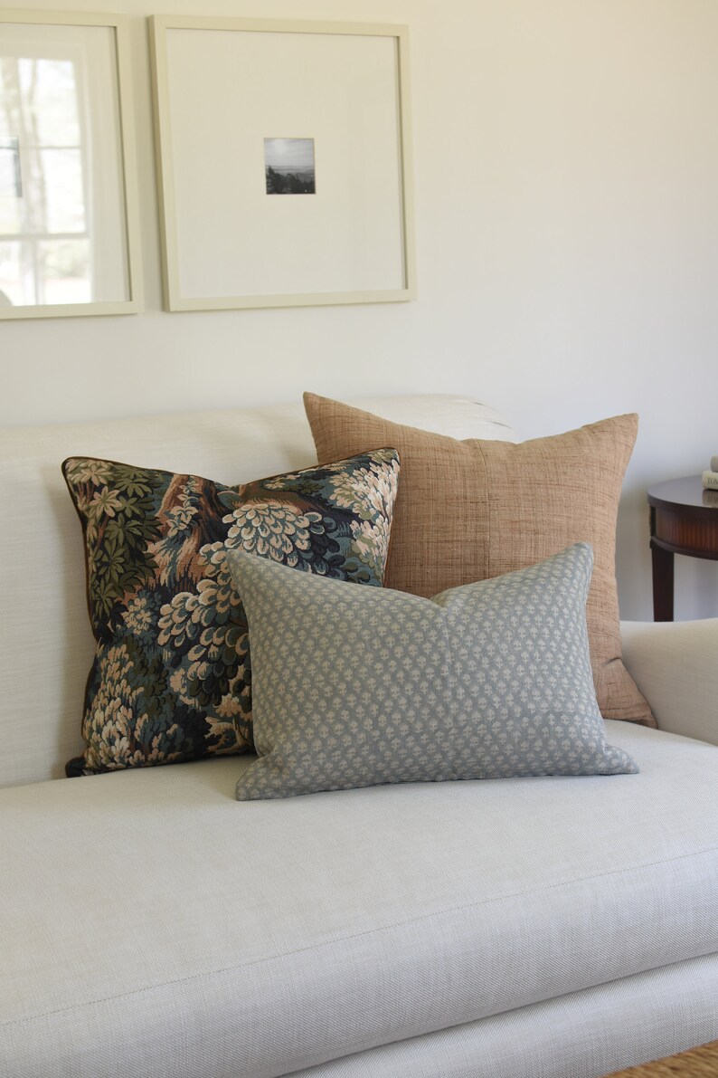 May include: A white couch with three throw pillows. The pillows are a patterned floral design, a solid brown, and a light blue with a small geometric pattern.